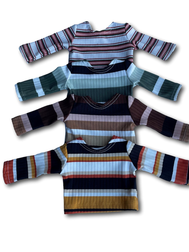 May include: Four striped long-sleeved shirts in different color combinations. The shirts are stacked on top of each other, with the bottom shirt being a black, white, orange, and brown striped shirt.