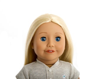 Op de afbeelding: Een blonde pop met blauwe ogen die een grijs overhemd met kraag draagt.