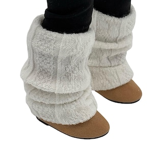 Può includere: Scaldamuscoli bianchi a maglia a treccia, sovrapposti e indossati sopra leggings neri. Gli scaldamuscoli sono abbinati a scarpe in camoscio marrone. L'immagine è su sfondo bianco. Accessorio invernale.