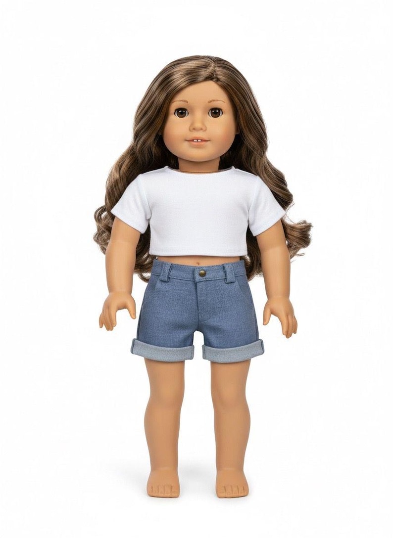 May include: A doll with long brown hair, wearing a white crop top and denim shorts. The doll has brown eyes and is standing against a white background. The shorts have rolled-up cuffs.