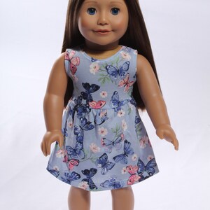 May include: A blue sleeveless dress with a butterfly print for a doll. The dress has pink and blue butterflies on a light blue background.