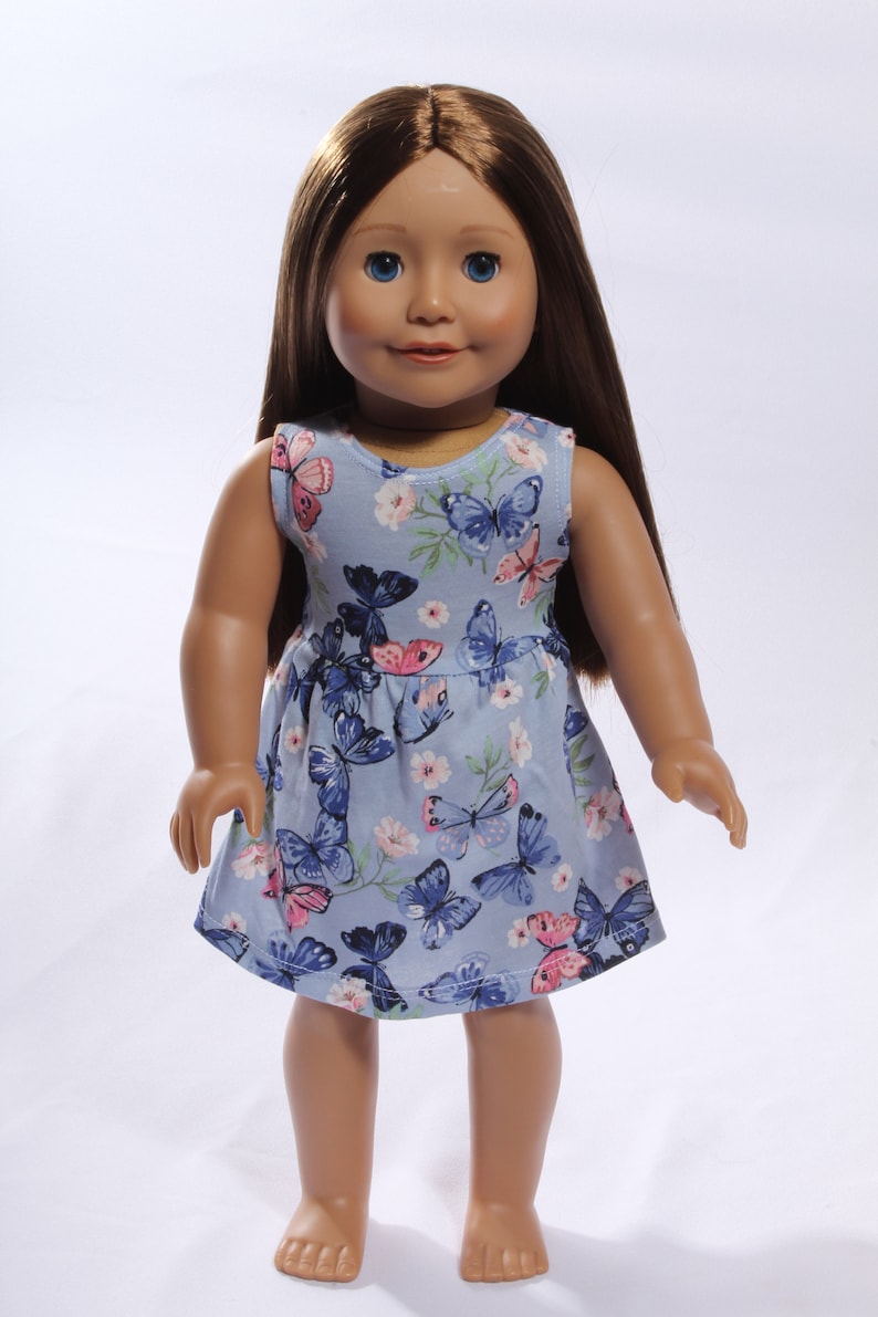 May include: A blue sleeveless dress with a butterfly print for a doll. The dress has pink and blue butterflies on a light blue background.