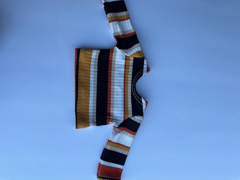 May include: A long-sleeved striped shirt with brown, black, white, and red stripes. The shirt has a round neckline.