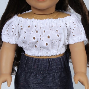 May include: A white off-the-shoulder doll top with eyelet detailing. The top has short, puffed sleeves and a fitted bodice.