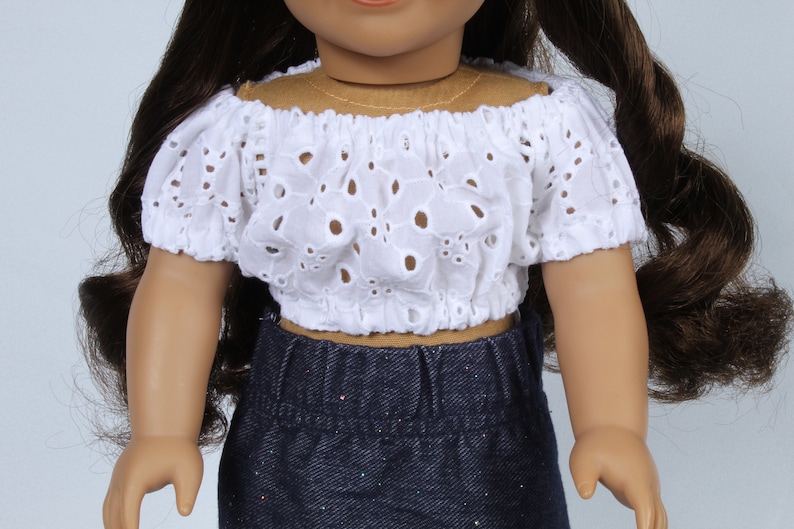 May include: A white off-the-shoulder doll top with eyelet detailing. The top has short, puffed sleeves and a fitted bodice.