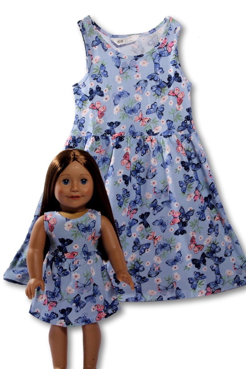 May include: A blue sleeveless dress with a butterfly and floral print. The dress has a gathered skirt and is shown on a doll and a larger size.