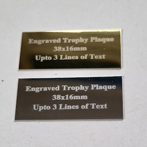 May include: Two engraved trophy plaques, one gold and one silver, with the text "Engraved Trophy Plaque 38x16mm Upto 3 Lines of Text".