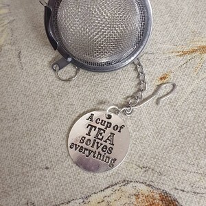 May include: Silver tea infuser with a chain and a charm that reads "A cup of TEA solves everything".