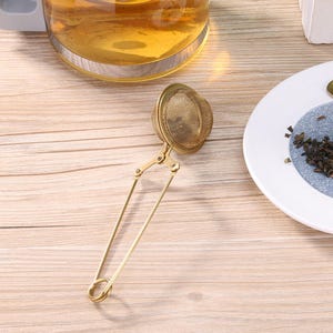 May include: A gold-coloured tea infuser with a round mesh ball and a long handle. The infuser is designed to be used with loose leaf tea.