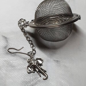 May include: A silver tea infuser with a chain and an elephant charm. The infuser is a sphere with a fine mesh.