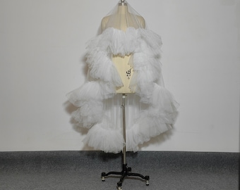 May include: A white tulle bridal veil with multiple layers of ruffles. The veil is displayed on a mannequin.