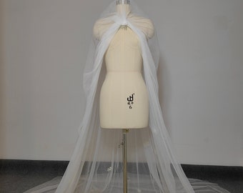 May include: A white tulle wedding veil with a cape style and delicate floral embroidery. The veil is draped over a dress form.