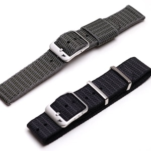 May include: Two watch straps, one gray and one black, are displayed against a white background. Both straps have a woven texture and stainless steel buckles. The gray strap has a subtle plaid pattern, while the black strap is solid.