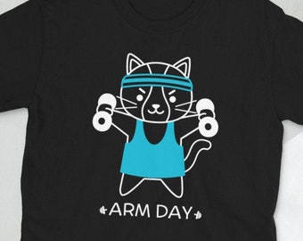 May include: Black t-shirt with a white outline of a cat wearing a blue tank top and headband, lifting dumbbells. The text "#ARM DAY#" is below the cat.
