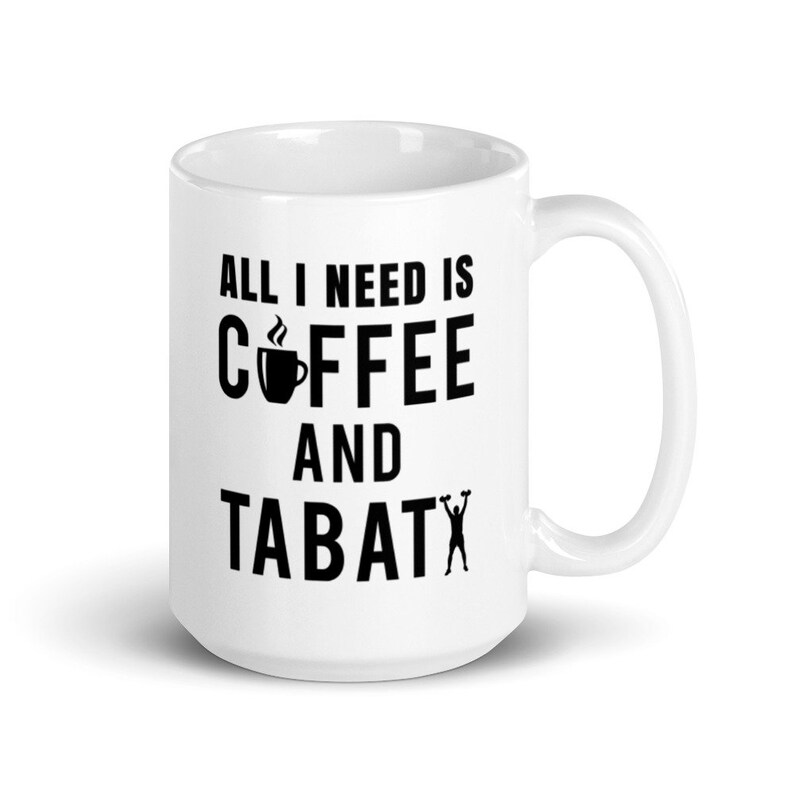 May include: White ceramic coffee mug with the text "ALL I NEED IS COFFEE AND TABATA" in black. The word "coffee" features a coffee cup icon. The mug has a curved handle.