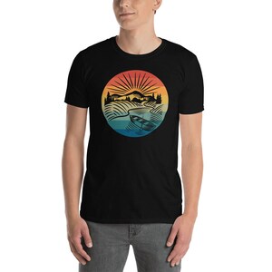 Pode incluir: Camiseta preta com um gr&aacute;fico retro de uma paisagem montanhosa com um rio e uma canoa. O gr&aacute;fico est&aacute; em tons de amarelo, laranja, vermelho, azul e verde.