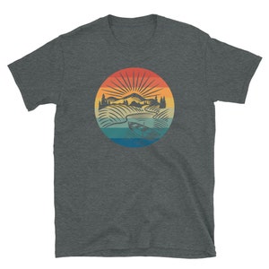 Pode incluir: Uma camiseta cinza escura mesclada com um gr&aacute;fico vintage de uma cena de lago com um barco. O gr&aacute;fico apresenta um p&ocirc;r do sol com cores laranja, amarelo e azul.