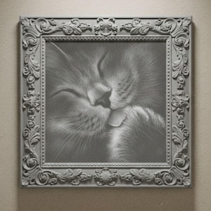Puede incluir: Una impresión en escala de grises enmarcada de la cara de un gato, con los ojos cerrados y la nariz tocando su boca. El marco gris claro presenta detalles ornamentados y arremolinados. La obra de arte está centrada sobre un fondo neutro.