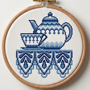 May include: A cross-stitch embroidery of a blue and white tea set, including a teapot and teacup, on a table with a decorative edge. The embroidery is set in a wooden hoop.