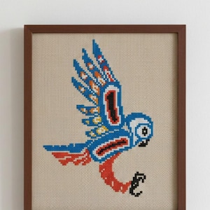 Puede incluir: Imagen de punto de cruz de un pájaro azul estilizado con las alas extendidas, enmarcado en un marco de madera marrón. El pájaro presenta detalles rojos, blancos y amarillos. El fondo es de tela beige.