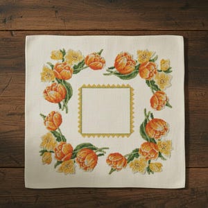 Puede incluir: Paño bordado cuadrado, de color crema, con un diseño floral. El bordado presenta tulipanes naranjas y flores amarillas dispuestas alrededor de un cuadrado central. El borde del cuadrado es de color dorado festoneado.