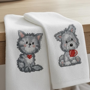 May include: Two white hand towels with cross-stitched animal designs. One towel features a gray cat with a red heart, the other a gray dog holding a red mug. The towels are made of a textured fabric.