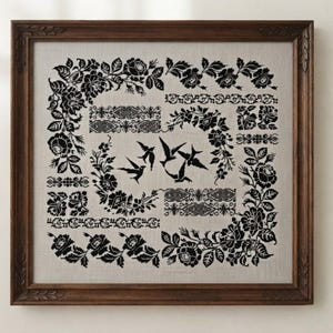 May include: A square framed cross-stitch embroidery featuring black thread on a light beige fabric. The design includes intricate floral borders, geometric patterns, and a central motif of four flying birds, all enclosed in a dark wood frame.