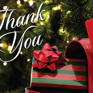 May include: A red mailbox with a red flag on top. A red and green striped gift box with a red bow is sticking out of the mailbox opening. The background is a blurry image of a Christmas tree with lights.