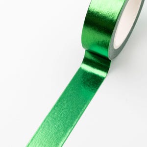 Può includere: Un rotolo di nastro adesivo color verde smeraldo vibrante con una finitura metallica liscia e riflettente. Il nastro è parzialmente srotolato, mostrando un colore verde brillante e uniforme sulla superficie e un nucleo in cartone bianco.