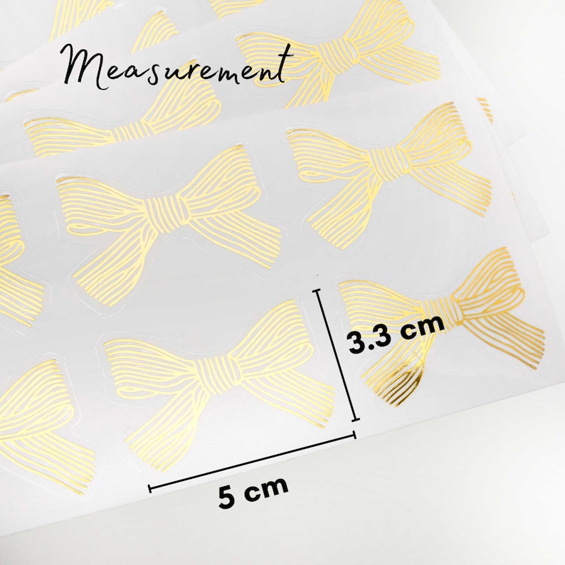 Pu&ograve; includere: Un foglio di adesivi trasparenti con fiocchi a linee dorate. Gli adesivi sono disposti a griglia. Un grafico di misurazione indica che i fiocchi sono larghi 5 cm e alti 3,3 cm. La parola Measurement &egrave; stampata nella parte superiore.