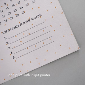 May include: A white calendar page with gold confetti printed on it. The calendar page has the numbers 8, 9, 14, 15, 16, 17, 21, 22, 23, 24, 25, 26, 7, 28, 29, 30, and 31 printed on it. The text "TOP 5 GOALS FOR THE MONTH" is printed at the top of the page. There are five blank lines below the text for writing goals. The text "can print with inkjet printer" is printed at the bottom of the page.