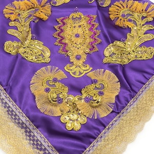 May include: A purple satin fabric square with gold and purple embroidery and sequins. The fabric has a gold lace trim around the edges.