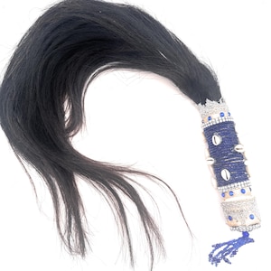 May include: A black hair accessory with a decorative handle. The handle is adorned with blue beads, small seashells, and silver accents. A blue tassel hangs from the bottom. The hair is long and flowing.