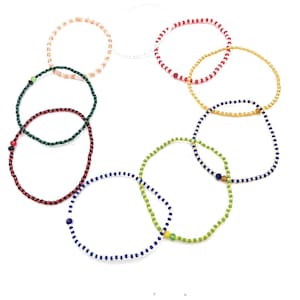 May include: Set of eight beaded bracelets in various colors, including red, green, blue, yellow, white, and black. The bracelets are made of small, round beads and are arranged in a circle.