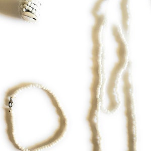 May include: A set of two white beaded necklaces, one long and one short. The shorter necklace has a silver clasp.