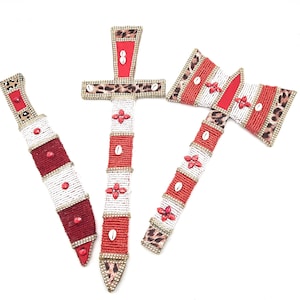 May include: Three decorative swords made of beads and fabric. The swords are red, white, and gold with a leopard print design.