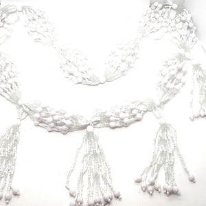 May include: White beaded garland with multiple strands and tassels. The garland is made of small white beads and has a delicate, feminine look.