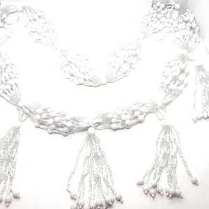 May include: A white beaded necklace with multiple strands and tassels. The necklace is made of small, round beads and has a delicate, feminine look.