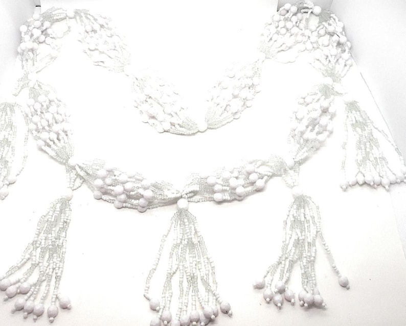 May include: A white beaded necklace with multiple strands and tassels. The necklace is made of small, round beads and has a delicate, feminine look.