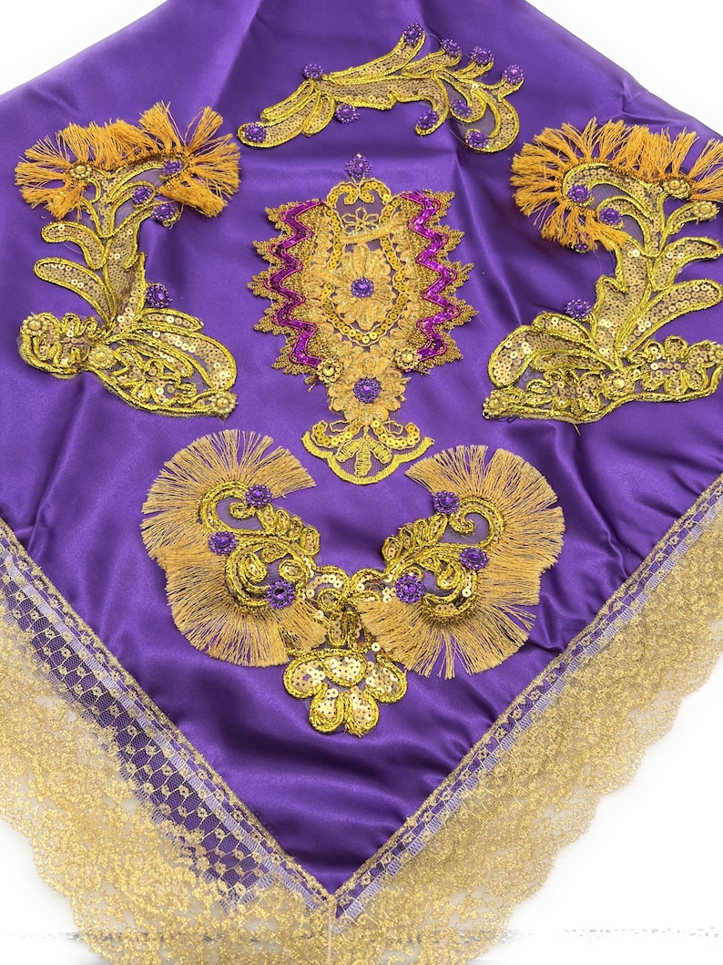 May include: A purple satin fabric square with gold and purple embroidery and sequins. The fabric has a gold lace trim around the edges.