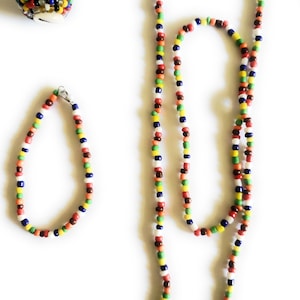 May include: A set of colorful beaded jewelry, including a necklace, bracelet, and ring. The beads are arranged in a repeating pattern of red, orange, yellow, green, blue, and white.