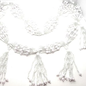 May include: White beaded garland with multiple strands and tassels. The garland is made of small white beads and has a delicate, feminine look.