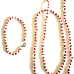 May include: A set of two red and white beaded necklaces. The larger necklace is longer and the smaller necklace is shorter. Both necklaces are made of small, round beads.