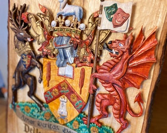 May include: A wooden plaque with a carved coat of arms. The coat of arms features a shield with a red and gold design, a deer, a dragon, and a crown. The plaque is inscribed with the text "Amor Veritas Veritas Amor De Vere-Austin of Delvin".