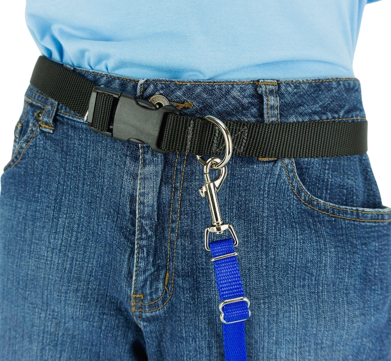 K&ouml;nnte beinhalten: Schwarzer Nylon-G&uuml;rtel mit Kunststoff-Schnalle, getragen mit blauer Jeans. Ein silberner Metallclip ist am G&uuml;rtel befestigt und mit einem blauen Nylonband verbunden. F&uuml;r freih&auml;ndiges Gassi gehen.