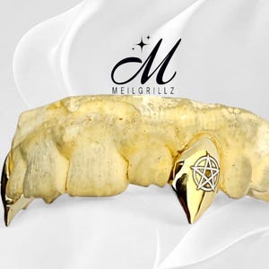 May include: Gold-coloured custom teeth grill with a pentagram design on one tooth. The grill is displayed against a white background with the text "MEILGRILLZ" and a stylized "M" logo.