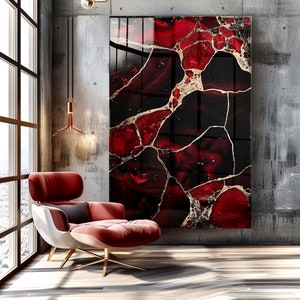 May include: Large abstract wall art featuring a striking design of red and black marble with gold veining. The artwork is displayed in a modern living space with a red armchair and a large window.