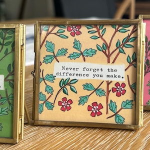 Peut inclure: Trois cadres carrés avec des motifs floraux et le texte "Never forget the difference you make." Les cadres sont dorés, et les fonds sont verts, jaunes et roses. Chaque cadre mesure environ 10 cm x 10 cm.