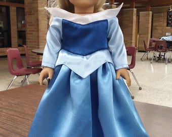 Puede incluir: Un vestido azul y blanco con cuello blanco y mangas largas. El vestido tiene un corpiño azul y una falda azul claro. El vestido está hecho para una muñeca.