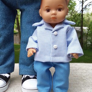 May include: A doll wearing a blue and white checkered shirt and blue pants. The doll is standing in front of a person wearing blue jeans and black and white sneakers. The doll's outfit has white buttons. The website address www.Etsy.com/shop/BibaDollClothes is visible.
